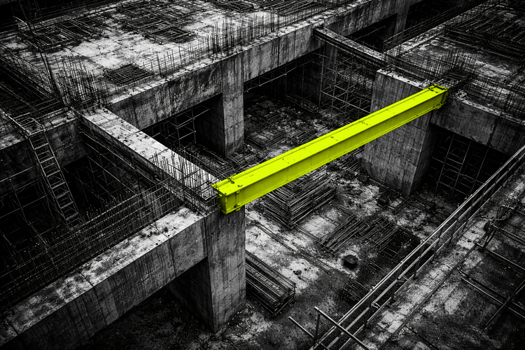 Black and white aerial view of an industrial construction site with a single acid yellow structural beam cutting through raw concrete and steel.